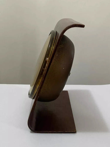 Side view of an antique wooden desk clock with a curved stand and brass clock face details