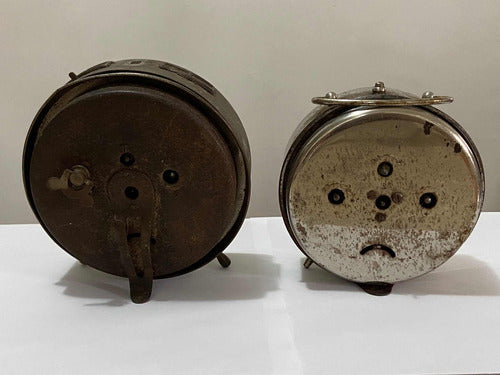 Back view of two vintage silver-colored old-fashioned alarm clocks on a white surface with worn details